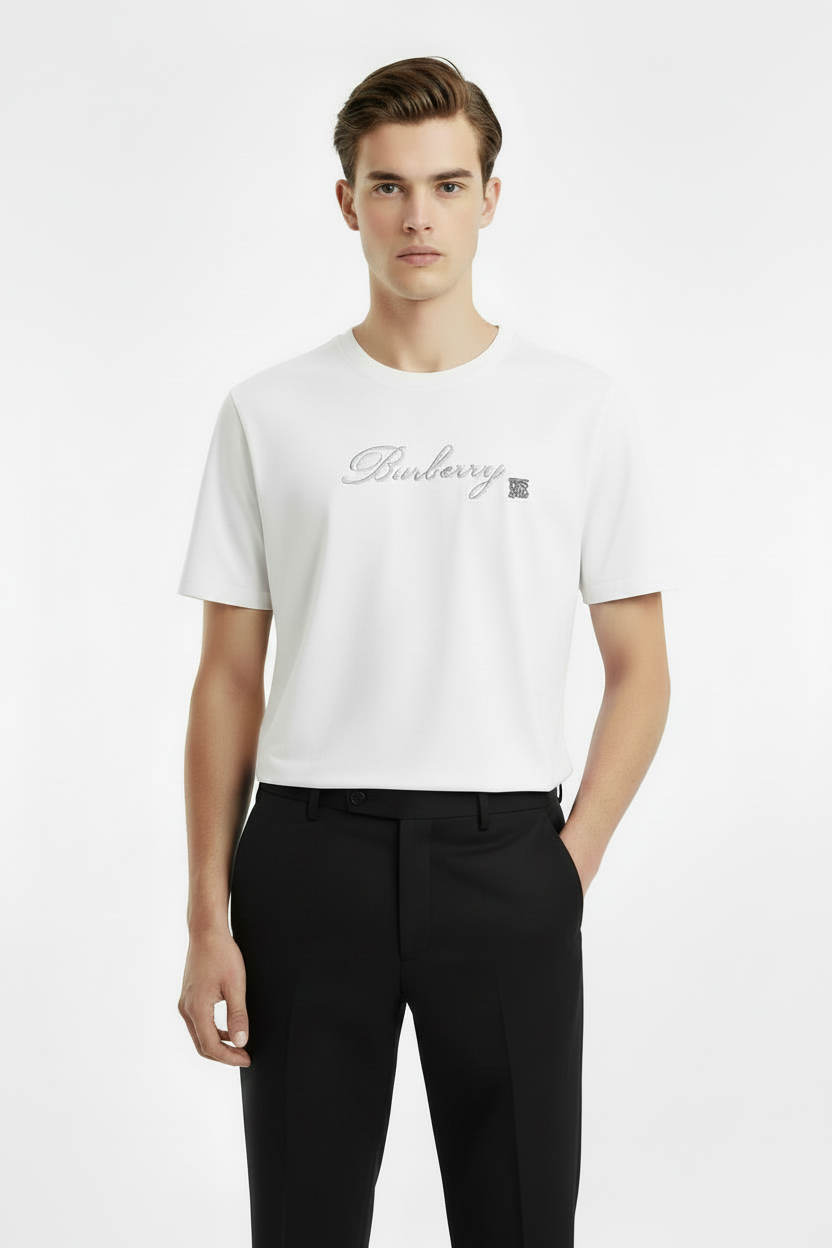 A white short-sleeve crewneck t-shirt featuring a silver cursive 'Burberry' logo and the iconic interlocking 'TB' monogram on the chest, displayed against a solid white background.
